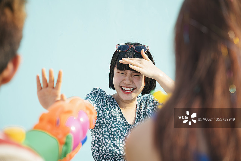 年轻的亚裔泰国人被水枪击中。人们向女孩喷水。泼水节。孤立在白蓝色。图片素材