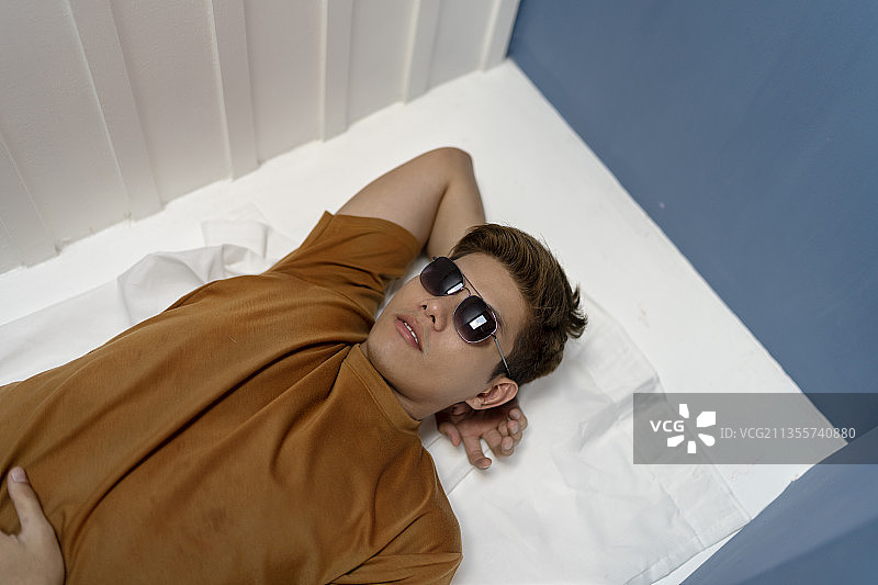 年轻英俊的亚洲泰国男子戴着太阳镜躺在垫子上仰望天空。在海滩上度假。日光浴。图片素材
