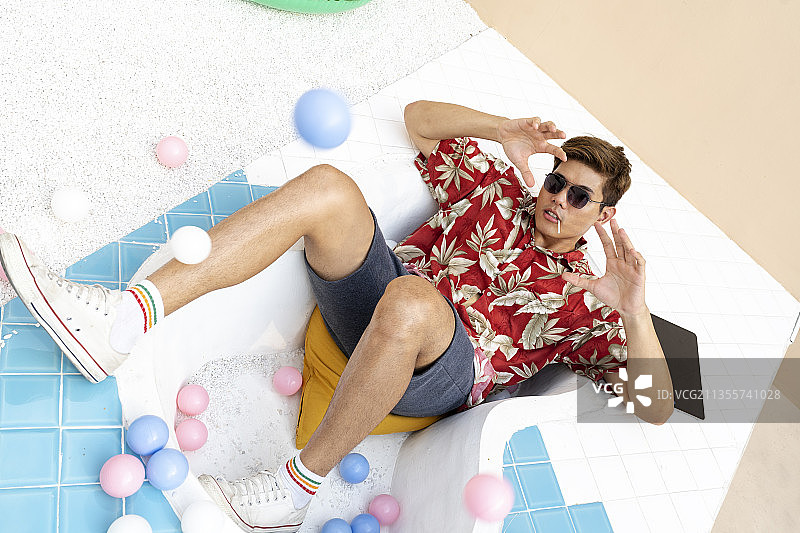 年轻英俊的亚洲泰国男子全身肖像穿着夏威夷衬衫和太阳眼镜躺在游泳池。色彩缤纷的夏日时尚肖像。图片素材