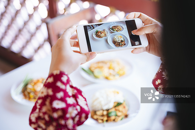 在餐厅里，穿着红衬衫的女人用智能手机拍下桌上的食物。图片素材