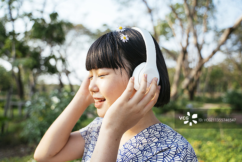 亚洲女人波波发型封闭eY在自然公园户外用白色耳机听音乐。图片素材
