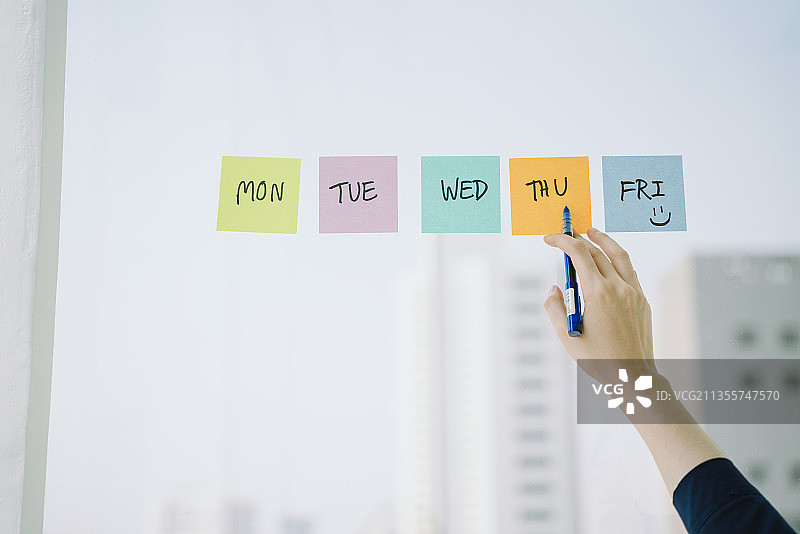 美丽的亚洲年轻的泰国女人长黑头发制作时间表在粘纸笔记在玻璃墙上。商人安排会议。图片素材
