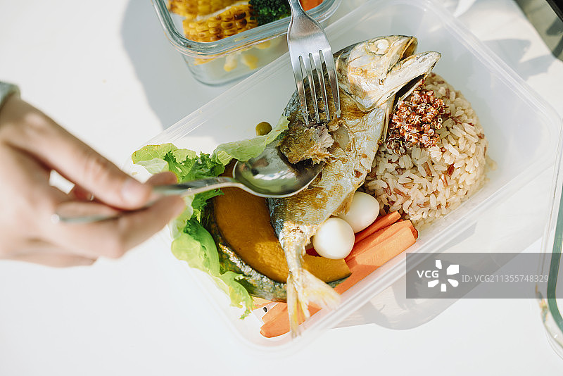 俯视图的人吃油炸鲭鱼和米饭与健康的新鲜蔬菜。食品交付。午餐盒。图片素材