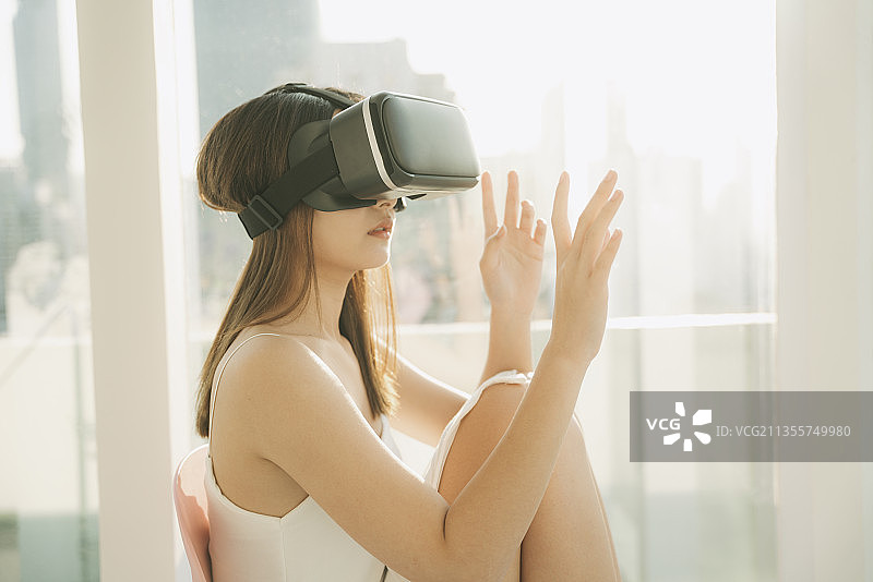 靠近美丽的亚洲泰国女人戴着虚拟现实头盔，玩虚拟现实游戏。游戏产业的技术。在摩天大楼的背景。图片素材