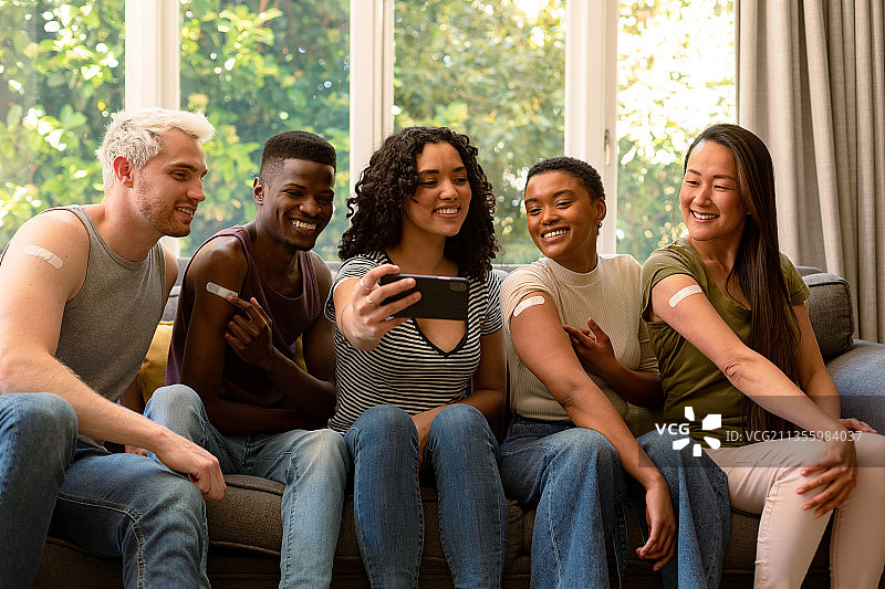 接种疫苗后展示创可贴并自拍的一群快乐的不同种族的男女朋友图片素材