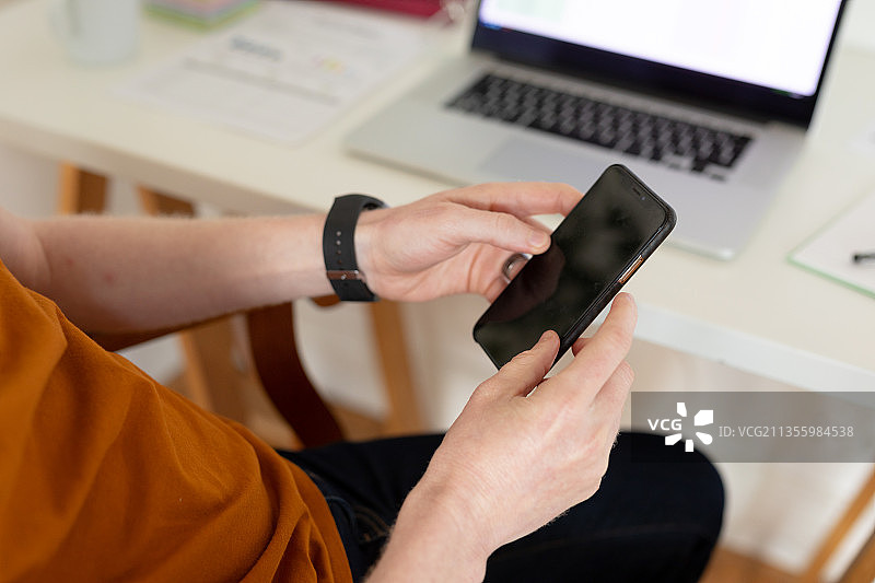 手持智能手机，背景为笔记本电脑的特写图片素材