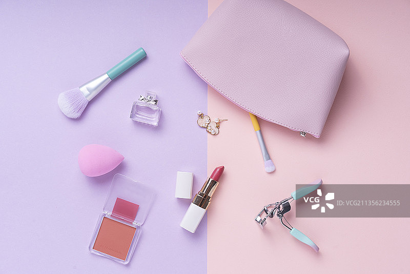 化妆品顶视图在淡粉色和紫色的桌子上。工作场所和化妆包。图片素材