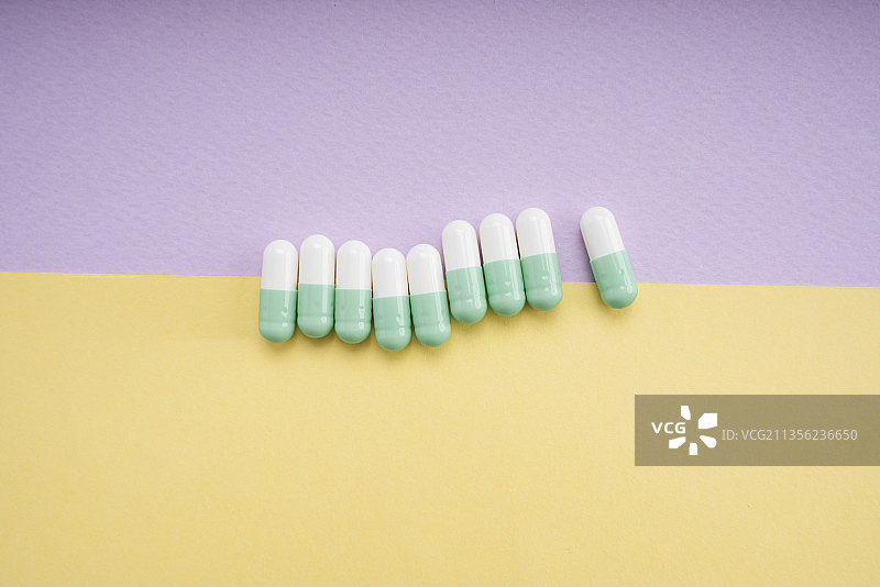 白色和浅绿色药丸胶囊在黄色和紫色的背景上。图片素材