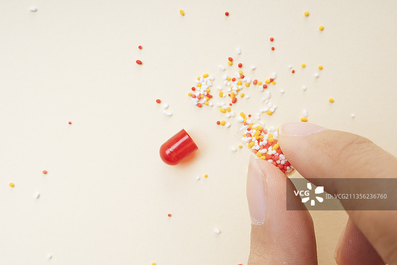 人的手抓住破碎的红色药丸胶囊和分子。图片素材