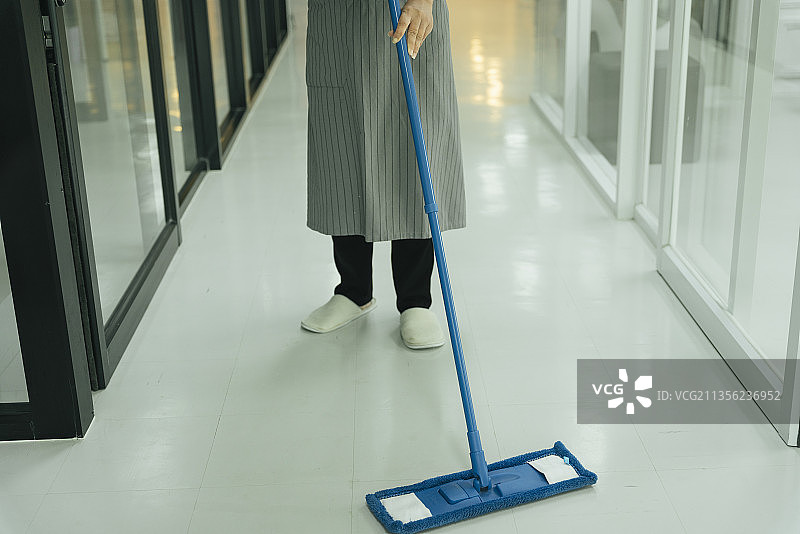 女佣用拖把清洁公寓房间的地板。图片素材