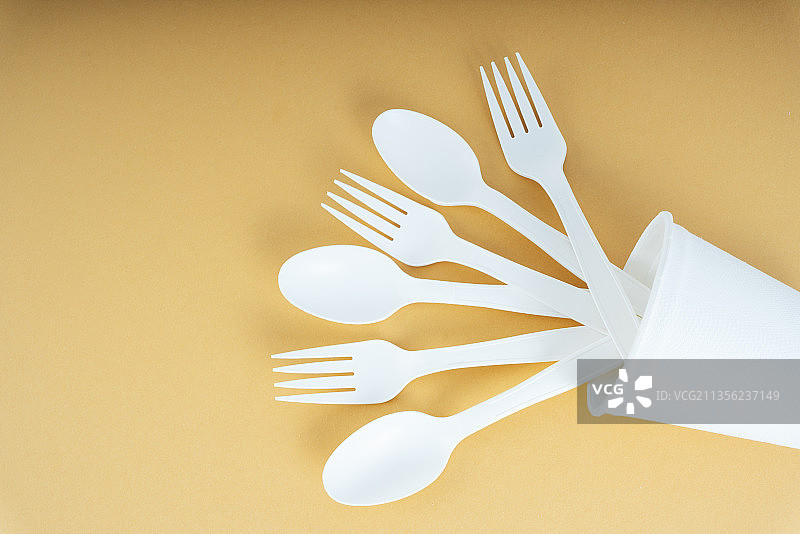 塑料勺子和叉子放在橙色背景的杯子里。一次性用具。图片素材