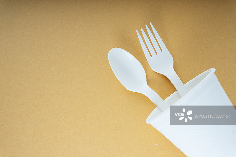塑料勺子和叉子放在橙色背景的杯子里。一次性用具。图片素材