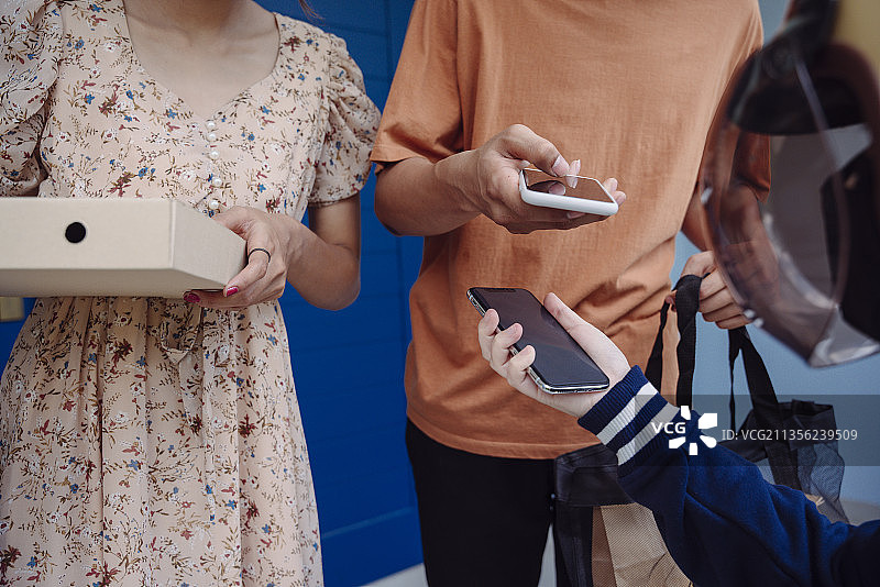 顾客夫妇用智能手机扫描码支付披萨外卖费用。图片素材