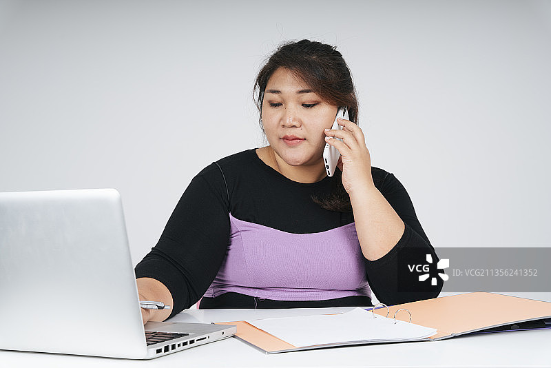 亚洲胖女商人工作在笔记本电脑和电话与客户图片素材