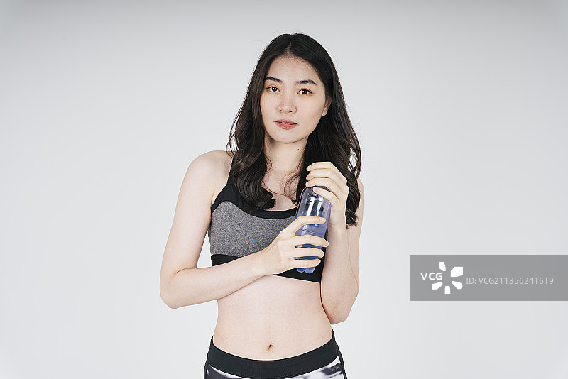 亚洲妇女灰色运动胸罩拿着塑料瓶水在白色背景。图片素材