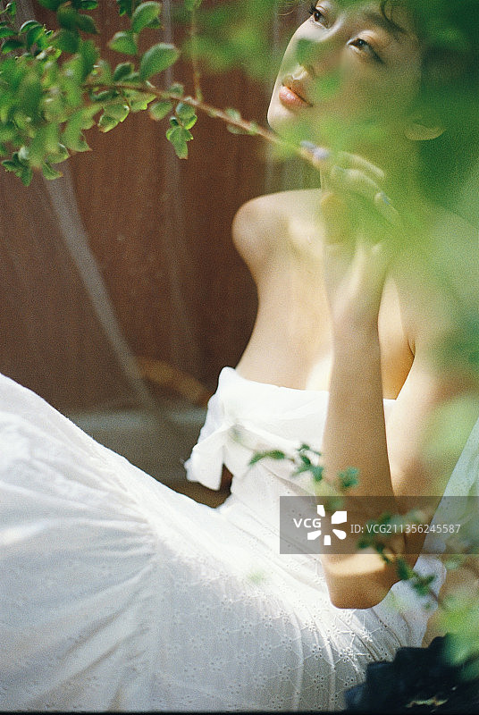 身穿白色连衣裙坐在植物旁的年轻女子，越南图片素材