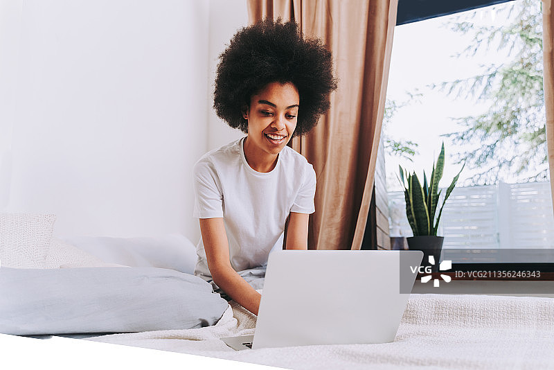 微笑的年轻女人在床上使用笔记本电脑图片素材