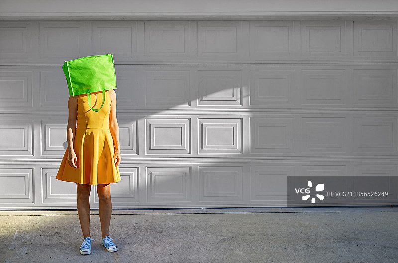 头戴绿色购物袋，身穿黄色连衣裙的女人图片素材