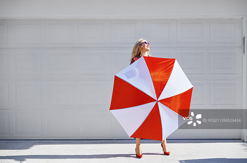 金发女人身穿紫红色连体裤站在红白雨伞后面图片素材