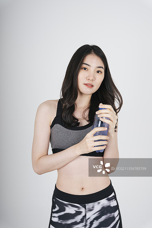 亚洲女人的肖像在运动胸罩装手持水瓶在白色的背景。图片素材