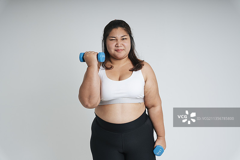 健康肥胖女性在白色运动胸罩锻炼与哑铃孤立在白色背景。图片素材