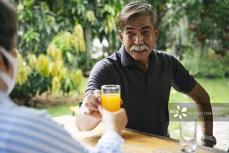 一位年长的老人在院子里给他的妻子一杯橙汁。图片素材