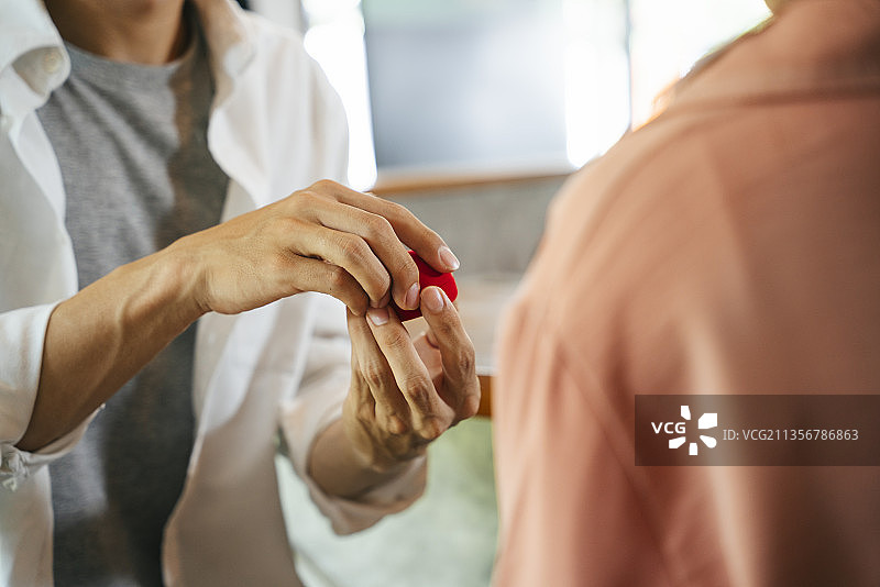 你愿意嫁给我吗?男人向女人求婚，并从红盒子里拿出订婚戒指。浪漫的建议。图片素材