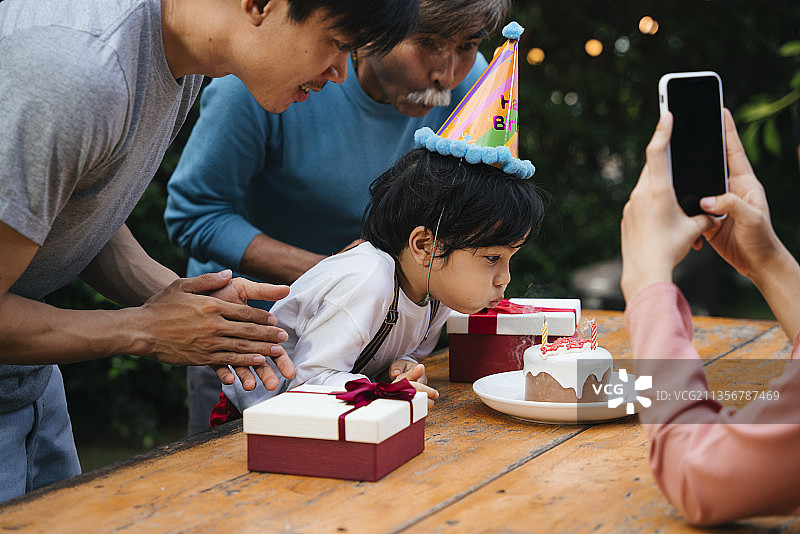 亚洲小孩吹蛋糕蜡烛和家人庆祝生日派对。图片素材