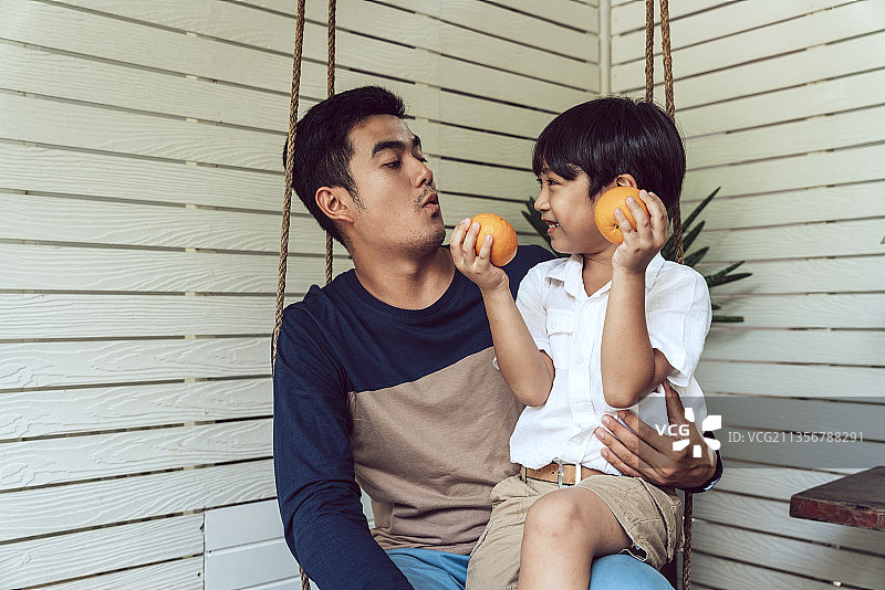 亚洲父亲和儿子喜欢在早餐或午餐吃橘子。图片素材