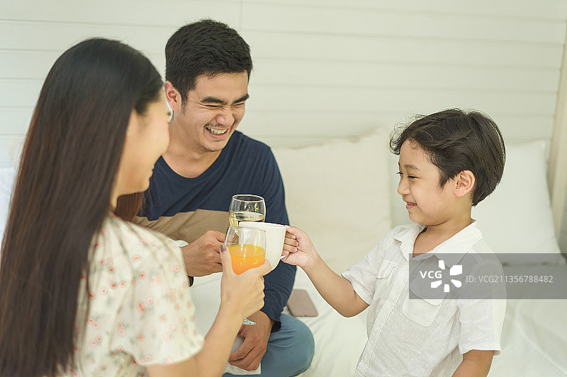 亚洲泰国家庭用健康饮料祝酒。牛奶和橙汁。一家人在家里一起吃早餐。图片素材