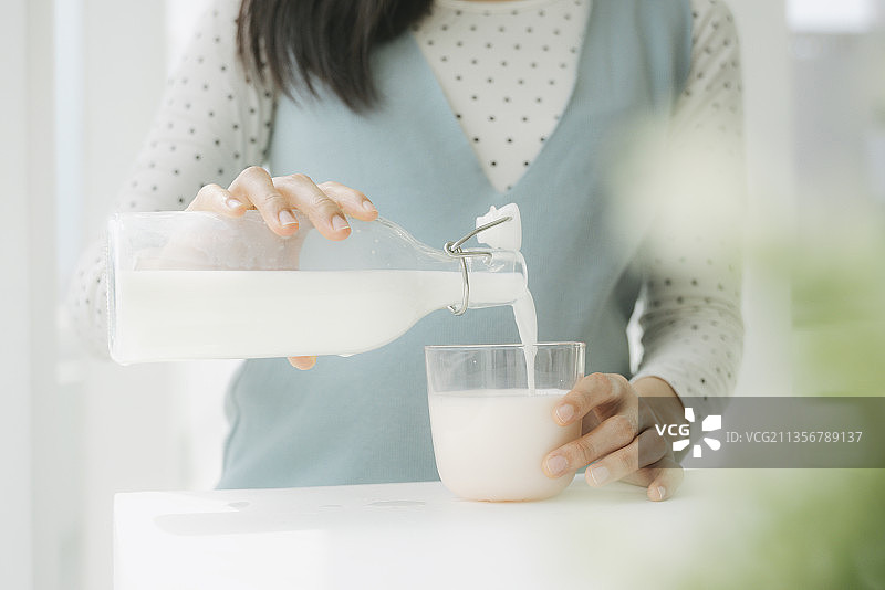 特写镜头-年轻美丽的亚洲孕妇从瓶子里倒出新鲜的牛奶。图片素材