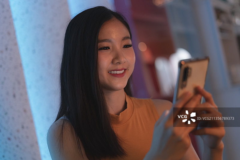 美丽的亚洲泰国女人在夜总会使用智能手机。图片素材