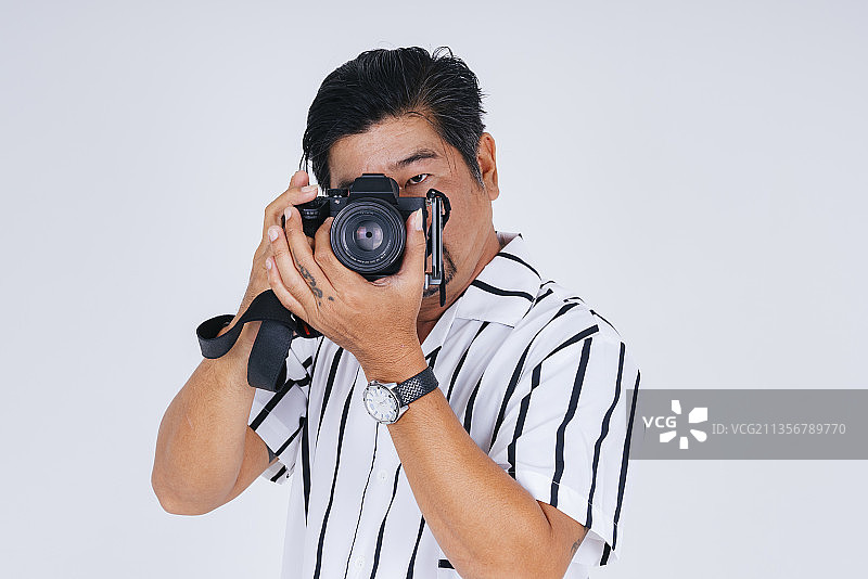 成年亚洲男子在白色衬衫作为摄影师与相机隔离在白色背景。图片素材