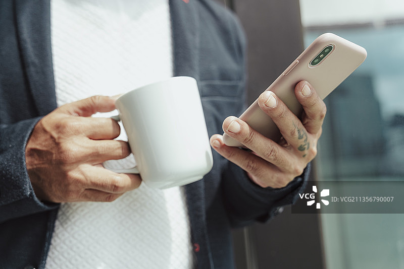 近-商人拿着咖啡杯和智能手机。图片素材