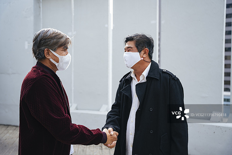 老人肖像，老人戴着口罩在户外握手。同意做生意。图片素材