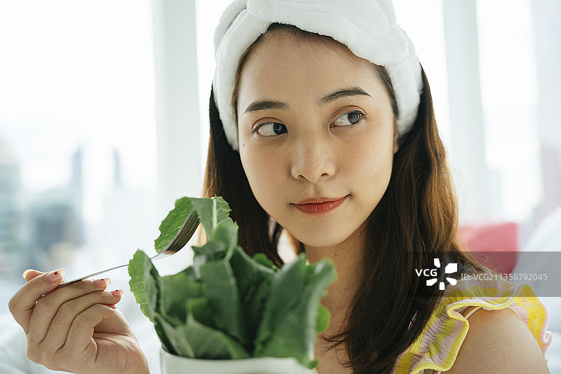 年轻的亚洲黑发女子与白色头巾喜欢吃有机蔬菜沙拉。图片素材