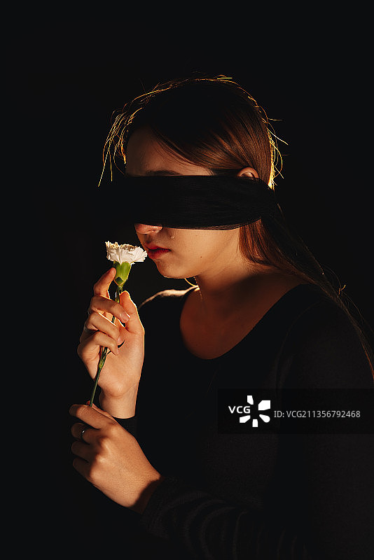 盲人折叠女人闻花隔离在黑色背景。图片素材