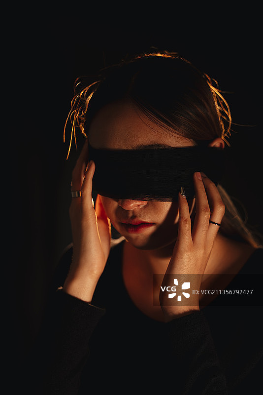 蒙住眼睛美丽的混血妇女隔离在黑色背景。图片素材