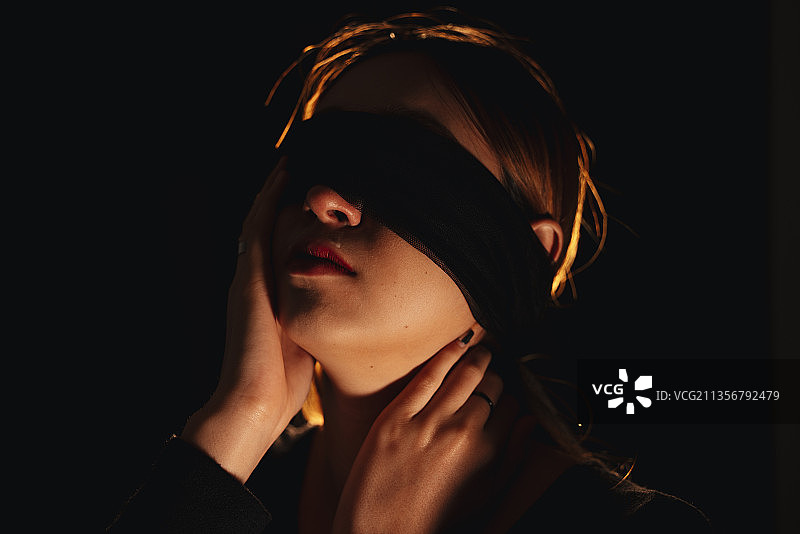 蒙住眼睛美丽的混血妇女隔离在黑色背景。图片素材