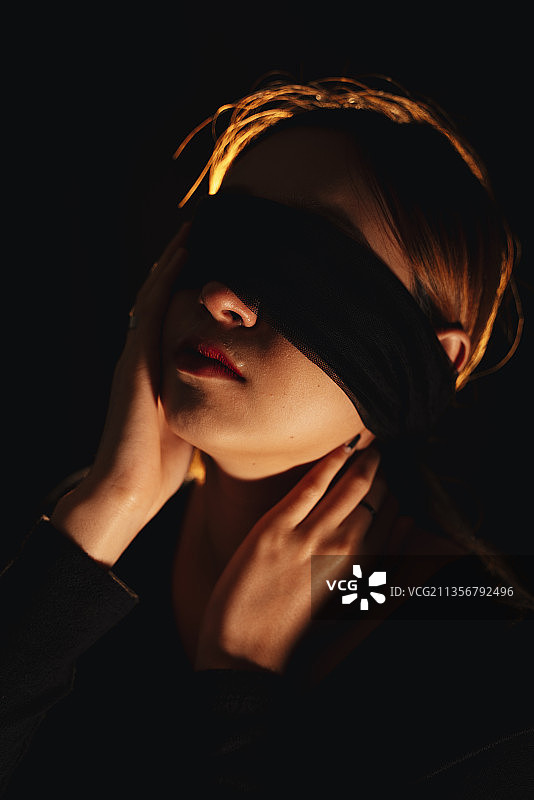 蒙住眼睛美丽的混血妇女隔离在黑色背景。图片素材