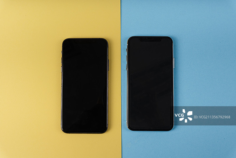 俯视图-两个智能手机屏幕模拟在黄色和蓝色背景。图片素材