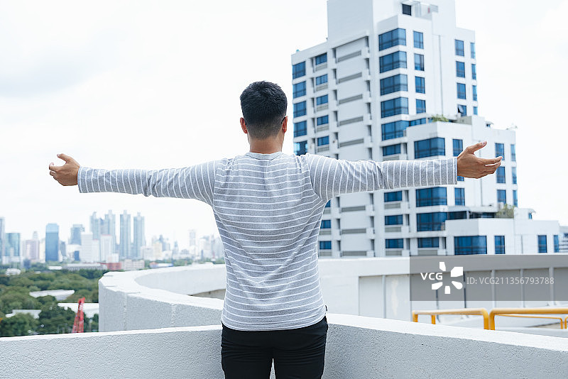 后视图-年轻人站在户外，双臂张开，自由自在。图片素材