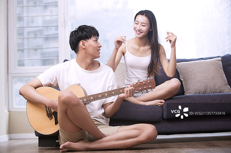 年轻男子在客厅为女朋友弹奏吉他图片素材