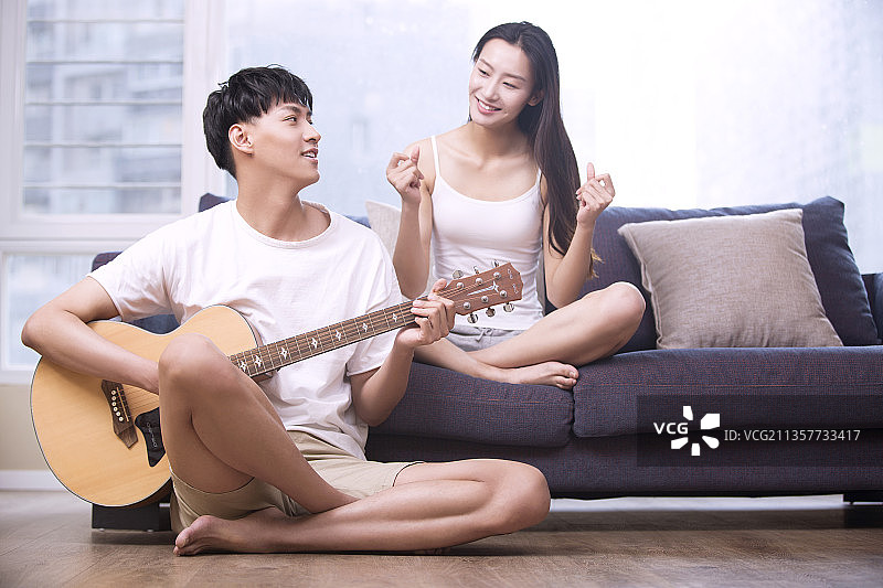 年轻男子在客厅为女朋友弹奏吉他图片素材