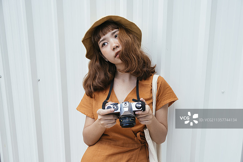 漂亮年轻的亚洲潮女穿着橙黄色的长裙卷发戴着帽子拿着相机。可爱的摄影师的女人。图片素材