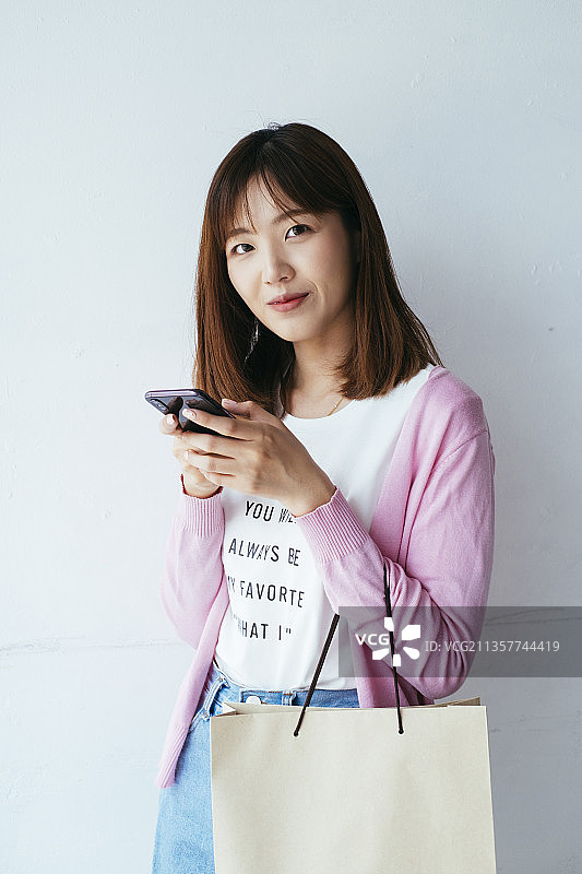 年轻的亚洲泰国女人在网上购物，拿着智能手机购物袋孤立在白色背景。图片素材