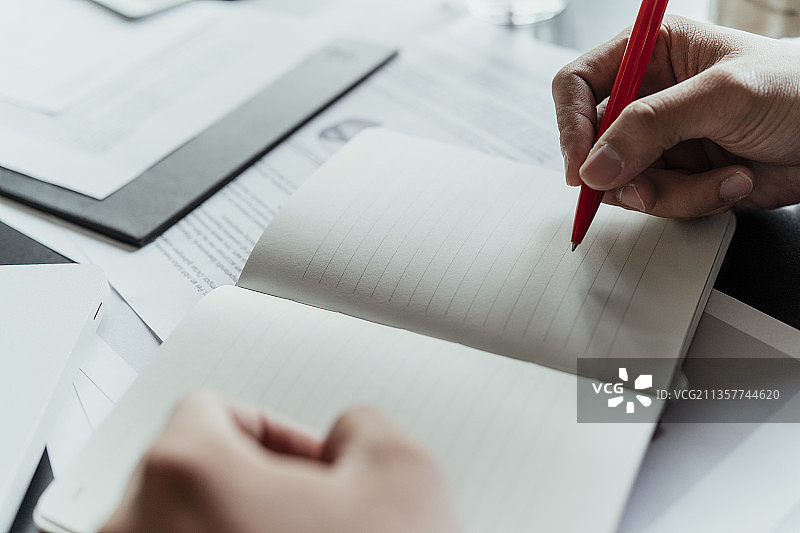 一个商人在会议室的记事本上做笔记的手。在现代办公室工作的人。商人、金融、会计工作、查帐、使用计算器和查找信息。图片素材