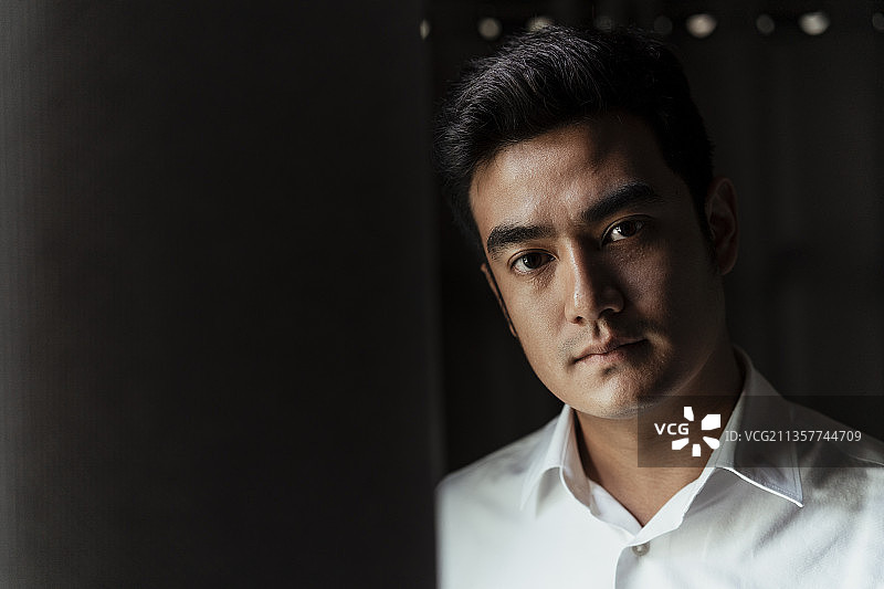 近距离的肖像成年亚洲泰国人穿着白领衬衫在黑暗的房间。图片素材