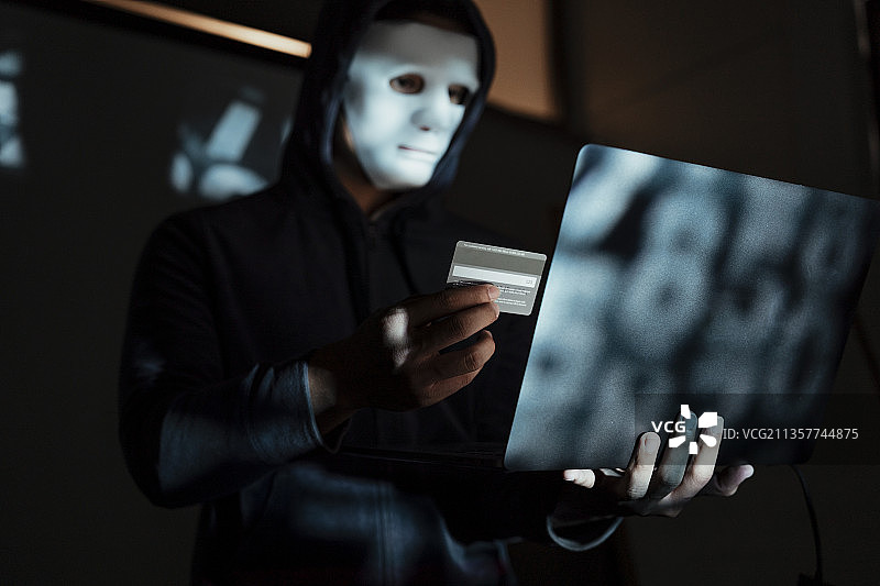 黑客在笔记本电脑上使用信用卡进行未经授权的购物。信用卡持有人未经授权的付款。黑客巢穴。钱砍。图片素材