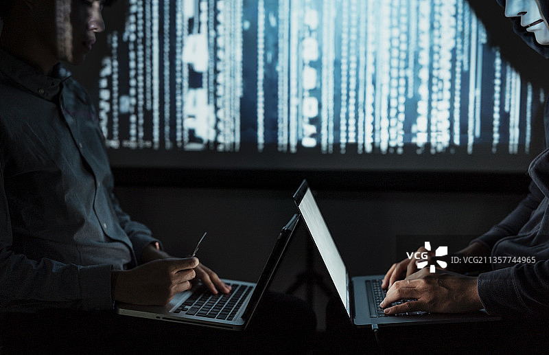 两个黑客在服务器室内用笔记本电脑一起工作。暗室系统入侵。日期黑客基地。图片素材